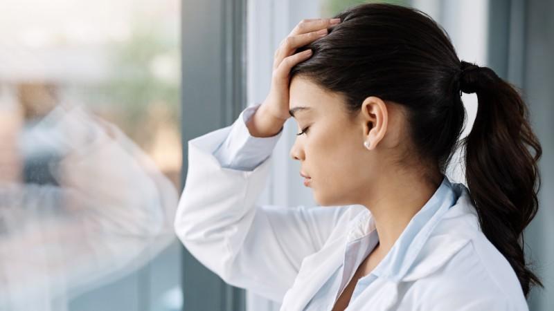 Overwhelmed doctor with her hand on her forehead looking out window